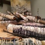 An image of the art installation The Botany of Sacrifice, featuring cut wooden logs wrapped in fabric and tied with cord
