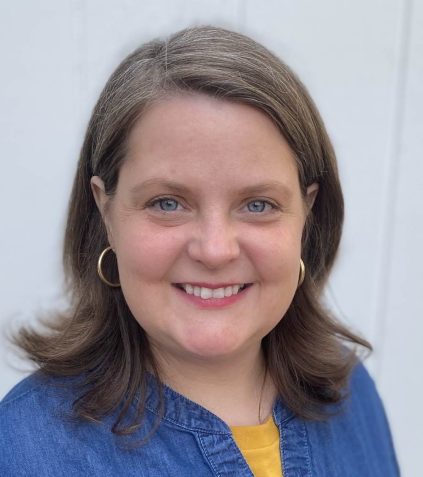 Susan smiles at the camera, wearing a blue shirt with a yellow accent.