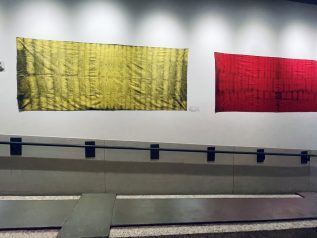 a large yellow and red tapestry patterned using natural materials hang along the length of a ramp leading to the IMRC kitchen/common area