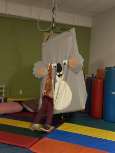 little girls legs sticking out of a sensory swing with a fabric wrap designed to look like a koala