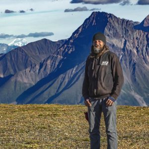 man in a black beanie and black hoodie and blue jeans standing in front of mountain range