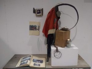 a collection of found objects assembled together to make a sculpture sit onto a table next to a photo album with some photos hung on the wall behind the table