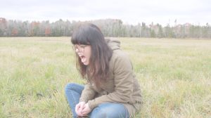 woman with long brown hair sitting in a grass field screaming